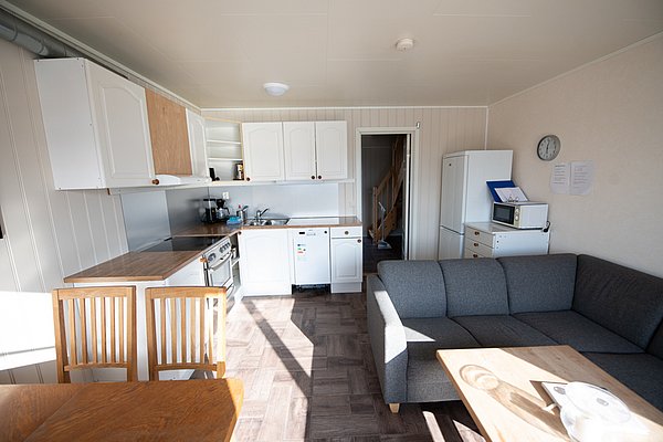 Gemütliche Ferienwohnung in Nordland, Norwegen, mit heller Küche, Holzstühlen, grauem Sofa und moderner Ausstattung. Ideal für Angler, die nach einem Abenteuer im Norden zurückkehren möchten. Perfekt für Angelreisen in atemberaubender Natur.