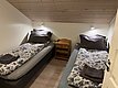 Gemütliches Schlafzimmer in Nord-Norwegen: Zwei Einzelbetten mit gemusterten Bettdecken, Holzdecke und Nachtschrank bilden eine einladende Unterkunft für Angler und Abenteurer. Entspannung nach einem erfolgreichen Angelurlaub.