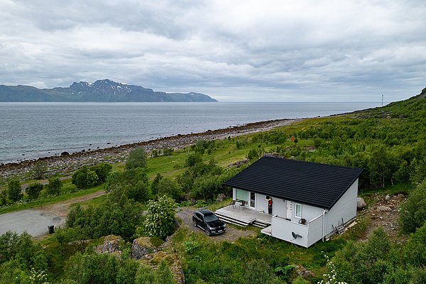 Gemütliches Ferienhaus am Fjord in Nord-Norwegen, umgeben von grüner Natur mit beeindruckenden Bergblicken und direktem Zugang zum Meer. Perfekter Ausgangspunkt für Angelabenteuer und Entspannung in malerischer Landschaft.