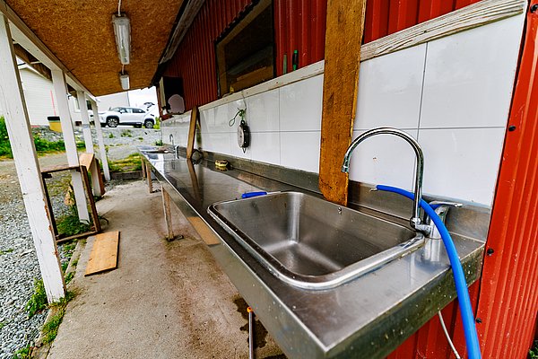 Edelstahl-Fischreinigungsstation in Nord-Norwegen mit Waschbecken und überdachtem Außenbereich. Ideal für Angelurlaube, bietet sie praktische Ausstattung zur Fischverarbeitung nach erfolgreicher Angeltour. Perfekte Kombination aus Funktionalität und authentischem Angelabenteuer.