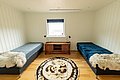 Gemütliches Zimmer in Nord-Norwegen mit zwei Einzelbetten, Holzboden und flauschigen Decken. Ein Fenster bietet Tageslicht, ein Teppich schmückt den Boden. Perfekt für entspannte Angelreisen in malerischer Umgebung.