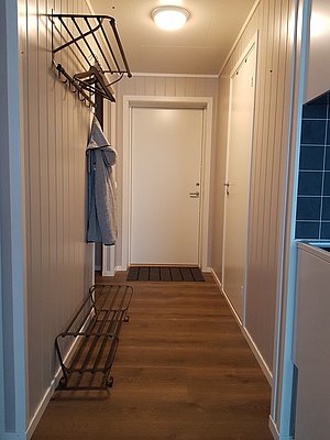 Flur in einem skandinavischen Haus in Nord-Norwegen: Holzverkleidete Wände, gefliester Boden, weiße Türen und Garderobe. Gemütliches, minimalistisches Design bietet eine einladende Atmosphäre. Ideal für Angelurlauber auf Entdeckungstour.