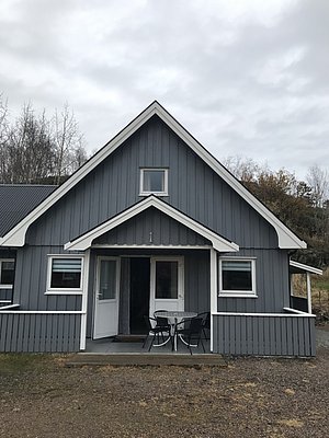 Graues Holzhaus in Hitra, Norwegen. Gemütliche Terrasse mit Sitzgelegenheit, umgeben von Natur. Ideal für Angelurlaube und Erholung. Perfekt für Abenteurer, die Norwegens ruhige Schönheit genießen wollen.