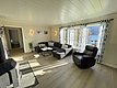 Helles Wohnzimmer in Nord-Norwegen mit gemütlicher Einrichtung, großem Ecksofa, Sessel und Kaminofen. Große Fenster bieten einen beeindruckenden Blick auf den Fjord. Perfekter Rückzugsort nach einem erfolgreichen Angelabenteuer im Norden.