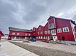 Rote Holzhäuser in Nord-Norwegen vor bewölktem Himmel. Traditionelle Architektur, ideal für Angelurlaube. Holzdielenweg, geparktes Auto, ruhige Atmosphäre. Perfekt für Abenteurer und Naturliebhaber. Entdecke die Schönheit der Region und genieße fischreiche Gewässer.