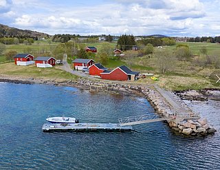Rote Holzhäuser am Ufer von Hitra, Norwegen, mit Anlegestelle und Boot. Malerische Landschaft ideal für Angelurlaube. Klare, blaue Küstengewässer bieten starke Fangchancen. Perfekt für ein entspanntes, dennoch abenteuerliches Reiseerlebnis.