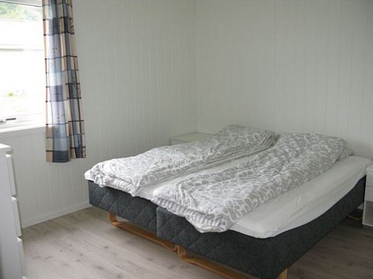 Helles Schlafzimmer in Nordland, Norwegen, mit gemütlichem Doppelbett, schlichten weißen Wänden und gemusterten Vorhängen. Ideal für Erholung nach einem spannenden Angelausflug. Perfekt für einen komfortablen Angelurlaub.