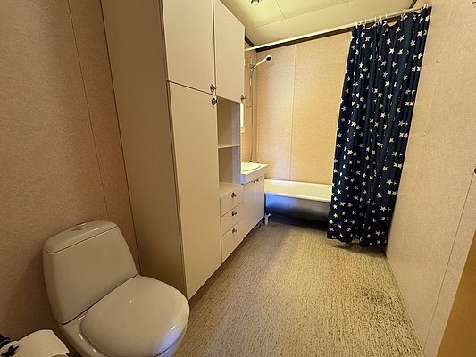 Modernes Badezimmer auf Hitra, Norwegen, mit Toilette, Waschbecken und Badewanne. Dezente Einrichtung und blauer Duschvorhang mit weißen Sternen sorgen für Komfort nach einem erlebnisreichen Angeltag.