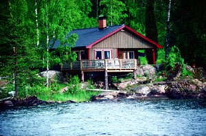 Ein rustikales Holzhaus am See in Värmland, Schweden, umgeben von üppiger Natur. Perfekter Rückzugsort für Angelreisen und Naturliebhaber. Veranda mit Seeblick, Pinien und Birken säumen das Ufer.