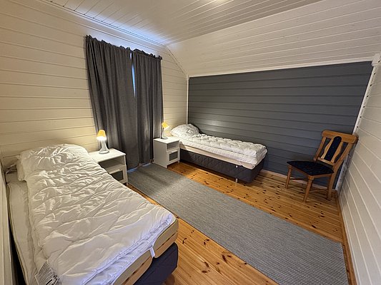 Gemütliches Schlafzimmer in Hitra, Norwegen, mit zwei Einzelbetten, heller Holzvertäfelung und modernem Design. Perfektes Angelurlaub-Domizil in ruhiger Umgebung. Ideal für Erholung nach erfolgreicher Angeltour.