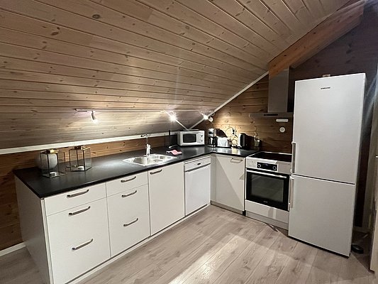Gemütliche Küche in Nord-Norwegen mit Holzwänden, moderner Ausstattung und Dachschräge. Inklusive Kühlschrank, Ofen, Spüle und Mikrowelle. Perfekt für Angelurlaube, um den Tagesfang frisch zuzubereiten. Ideale Unterkunft für Erholung und Abenteuer.