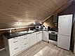 Gemütliche Küche in Nord-Norwegen mit Holzwänden, moderner Ausstattung und Dachschräge. Inklusive Kühlschrank, Ofen, Spüle und Mikrowelle. Perfekt für Angelurlaube, um den Tagesfang frisch zuzubereiten. Ideale Unterkunft für Erholung und Abenteuer.
