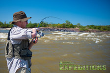 Ein Angler in Südwest-Norwegen hält die Angelrute angespannt, bereit für den großen Fang. Sonniges Wetter und sprudelndes Gewässer versprechen ein ideales Angelabenteuer. Perfektes Reiseziel für passionierte Angler.