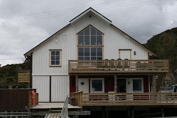 Ein traditionelles weißes Holzhaus mit Balkon in Nordland, Norwegen, umgeben von malerischer Natur. Ideal für Angelreisen und unvergessliche Urlaubserlebnisse in der nordischen Landschaft.