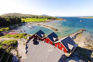 Luftaufnahme von roten Fischerhütten am Fjord in Nordland, Norwegen. Ruhige Buchten, klares Wasser und grüne Wiesen schaffen eine idyllische Angelkulisse. Perfekt für einen erholsamen Angelurlaub in atemberaubender Natur.