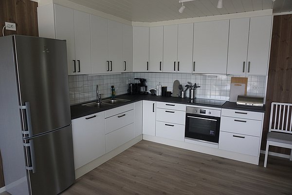 Eine moderne, gut ausgestattete Küche in Nordland, Norwegen, mit weißen Schränken, Edelstahlgeräten und Holzfußboden, ideal für gemütliche Angelurlaub-Unterkünfte. Perfekt ausgestattet für den Fang des Tages.