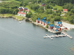 Luftaufnahme von Hitra, Norwegen: Malerische rote Hütten am Wasser, umgeben von üppiger Natur. Perfekter Angelurlaubsort mit Bootsanleger und ruhiger Atmosphäre für erholsame Auszeiten und Abenteuer.