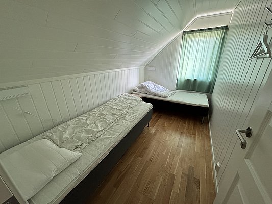 Gemütliches Schlafzimmer auf Hitra, Norwegen, mit zwei Einzelbetten, holzvertäfelten Wänden und Tageslicht. Perfekte Unterkunft für einen erholsamen Angelurlaub in der Natur. Ideal für Entspannung nach einem erfolgreichen Angeltag.