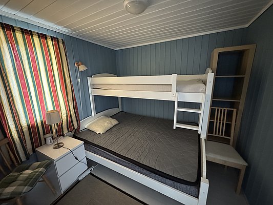 Gemütliches Schlafzimmer in Hitra, Norwegen, mit Etagenbett vor blau gestrichenen Wänden. Bunt gestreifte Vorhänge, Nachttischlampe, ideal für Angelurlauber. Perfekt für Entspannung nach einem erfolgreichen Tag am Wasser.