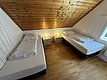 Gemütliches Schlafzimmer in Hitra, Norwegen, mit zwei Einzelbetten unter schräge Holzdecke. Weiße Wände, Holzboden und Nachttisch mit Lampen sorgen für eine einladende Atmosphäre. Ideal für Ruhesuchende nach einem Angeltag.
