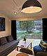 Gemütliches Wohnzimmer in Hitra, Norwegen, mit Fenstern zur Seelandschaft. Moderne Einrichtung, graues Sofa, Holztisch, sanfte Beleuchtung. Ideal für Angelreisen und naturverbundene Erholung. Perfekte Kulisse für Entspannung und Abenteuer gleichermaßen.