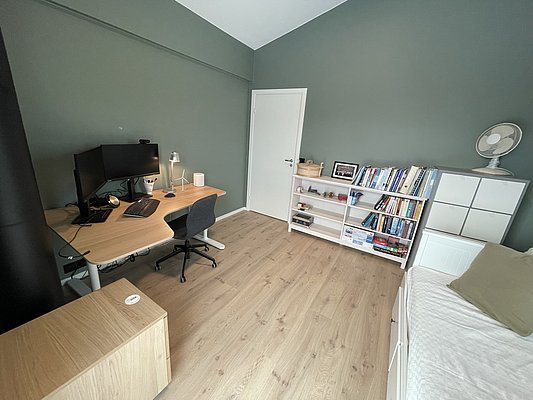 Helles, modern eingerichtetes Zimmer in Hitra, Norwegen: Holzfußboden, Schreibtisch mit Computer, Bücherregal, Bett und entspannende Atmosphäre – ideal für Angler nach einem aufregenden Angeltag. Perfekte Unterkunft für deinen Angelurlaub.