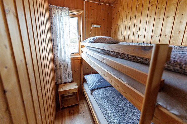 Kleines Schlafzimmer aus Holz mit einem Etagenbett und einem Fenster mit Vorhang in Hitra, Norwegen. Gemütliche Unterkunftsidee für Angelreisen. Ideal für Erholung nach einem erlebnisreichen Angeltag.