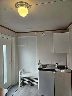 Heller, gemütlicher Innenraum in Nordland, Norwegen: kleine Küchenzeile mit Spüle, Herdplatte und Schrank, daneben eine Sitzbank unter hellem Licht. Ideal für einen entspannten Angelurlaub.