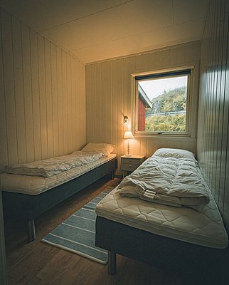 Gemütliches Schlafzimmer in Nordland, Norwegen, mit zwei Einzelbetten und warmem Licht. Ideal für Ruhesuchende und Angler, die komfortable Unterkünfte während ihrer Angelreise schätzen. Fenster mit Landschaftsausblick bietet zusätzliche Entspannung.