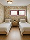 Gemütliches Schlafzimmer in Hitra, Norwegen: Zwei Einzelbetten mit beigen Bezügen, stilvolle Tapete mit goldenen Mustern, roter Fensterrahmen, Holzboden und Nachttisch mit Pflanze. Ideal für Erholung nach einem erfolgreichen Angeltag.