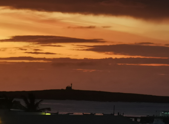 Sonnenuntergang über der Insel São Vicente in Kapverde: Dramatische, orangefarbene Wolken am Horizont, ruhiges Meer im Vordergrund, palmengesäumte Küste im Dunkel. Perfekt für Angelreisen und unvergessliche Naturmomente.