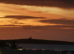 Sonnenuntergang über der Insel São Vicente in Kapverde: Dramatische, orangefarbene Wolken am Horizont, ruhiges Meer im Vordergrund, palmengesäumte Küste im Dunkel. Perfekt für Angelreisen und unvergessliche Naturmomente.