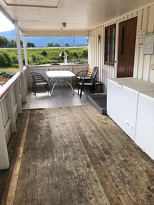 Überdachte Terrasse in Hitra, Norwegen, mit Holzboden, Tisch und Stühlen, ideal für Angelpausen. Die Umgebung bietet grünes Panorama und entspannten Rückzugsort. Perfekt für Deinen Angelurlaub in bezaubernder Naturkulisse.