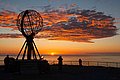 Eindrucksvolles Nordkap-Foto bei Sonnenuntergang in Nord-Norwegen: Berühmtes Globusmonument vor atemberaubender, tieforangefarbener Himmelsszenerie. Ideal für Nordlichter und Angelurlaube. Abenteuer in unberührter Natur erleben.