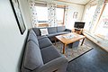 Gemütliches Wohnzimmer in Nordland, Norwegen. Helle, einladende Einrichtung mit großer grauer Eckcouch, Holztisch, Fernseher und dekorativen Vorhängen. Perfekt für entspannte Angelreisen und gemütliche Abende nach einem langen Tag am Wasser.
