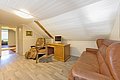 Gemütlicher Dachbodenraum in Nordland, Norwegen: Holztisch mit Stuhl, Ledersofa, heller Holzfußboden, sanft beleuchtet. Perfekt als ruhiger Arbeitsbereich in idyllischer skandinavischer Umgebung. Ideal für entspannte Angelreisen in Norwegen.