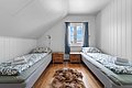 Gemütliches Schlafzimmer in Nord-Norwegen mit zwei Einzelbetten, Dachschräge, Holzboden und Fenster mit blauem Vorhang. Ein Fellteppich zwischen den Betten sorgt für rustikales Flair. Ideal für entspannte Angelurlaube.