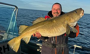 Ein Angler präsentiert stolz einen riesigen Kabeljau auf einem Boot in Norwegen. Perfektes Ziel für Angelreisen und Meeresangeln, um Abenteuerlust zu stillen und beeindruckende Fänge zu erleben. Petri Heil!