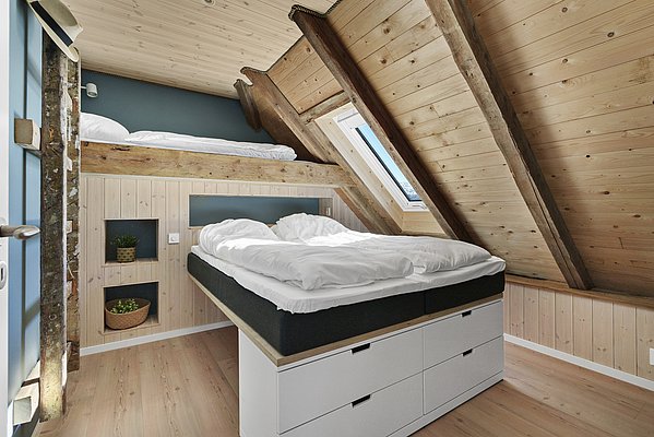 Gemütliches Schlafzimmer in Südwest-Norwegen mit hellem Holzinterieur, Dachschräge und Dachfenster. Zweckmäßige Einrichtung mit zwei Betten und Stauraum. Perfekt für Angelreisende auf der Suche nach Ruhe und Komfort in natürlicher Umgebung.