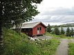 Rote Holzhütte in Nordland, Norwegen, umgeben von üppigem Grün und nah am Wasser. Ideal für Angelreisen, bietet Ruhe und malerische Ausblicke. Perfekt für Abenteuerlustige und Erholungssuchende.
