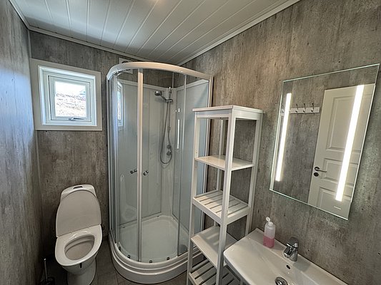 Modernes Badezimmer in Hitra, Norwegen, mit Dusche, WC und beleuchtetem Spiegel. Ideal für komfortable Angelreisen in skandinavischer Atmosphäre. Perfekte Unterkunft für Abenteurer und Erholungssuchende. Hell und funktional gestaltet.