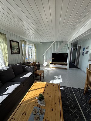 Gemütliches Ferienhaus in Hitra, Norwegen: Helle Holzverkleidung, große Fenster, komfortable Couch und Esstisch laden zum Entspannen nach einem erfolgreichen Angeltag ein. Perfekt für erholsame Angelurlaube in beeindruckender Naturkulisse.