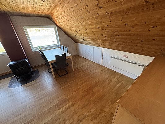 Gemütlicher Raum mit Holzboden und -decke in Hitra, Norwegen. Helles Fenster mit Ausblick, Esstisch mit zwei Stühlen. Perfekt für entspannte Angeltage in skandinavischem Ambiente. Ideal für Angelreisen und Erholung.