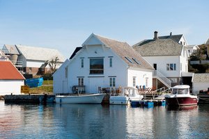 Weißes Fischerhaus am Wasser in Südwest-Norwegen, umgeben von Booten bei strahlendem Sonnenschein. Perfekt für Angelurlaub und Erholung in idyllischer skandinavischer Landschaft. Ideal für Naturliebhaber und Angler.
