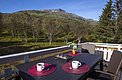Gemütliche Terrasse in Nord-Norwegen mit zwei Kaffeetassen auf einem Tisch, umgeben von üppigem Grün und Blick auf majestätische Berge. Perfekt für entspannte Angelurlaubsmomente in atemberaubender Naturkulisse.