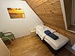 Gemütliches Schlafzimmer mit Holzwänden auf Hitra, Norwegen. Einzelbett mit frischer Bettwäsche, dekorativem Sonnenuntergangsbild und kleinem Nachttisch. Ideal für entspannte Angelreisen in malerischer Umgebung.