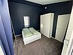 Gemütliches Schlafzimmer mit dunkelblauen Wänden auf Hitra, Norwegen. Doppelbett mit grüner Bettwäsche, weißem Schrank und kleinem Fenster. Ideal für erholsame Nächte nach einem erfolgreichen Angelurlaub.