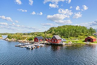 Küste in Hitra, Norwegen: Rote Häuser am Wasser, umgeben von grünen Wäldern und Booten am Steg. Perfekt für Angelreisen und Naturerlebnisse in idyllischer Fjordlandschaft.