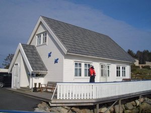 Gemütliches weißes Ferienhaus mit grauem Dach in Hitra, Norwegen. Einladende Veranda mit Blick auf die Natur, perfekt für Angelurlauber. Entdecke Hitra & Umgebung für dein nächstes Meeresangeln-Abenteuer!