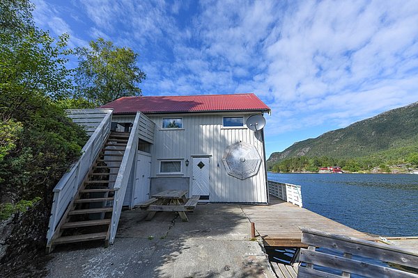 Gemütliches, weißes Ferienhaus mit rotem Dach direkt am Wasser in Hitra, Norwegen. Umgeben von grüner Landschaft und Bergen, ideal für Angelreisen und Outdoor-Abenteuer. Perfekt für Ruhe und Erholung in der Natur.